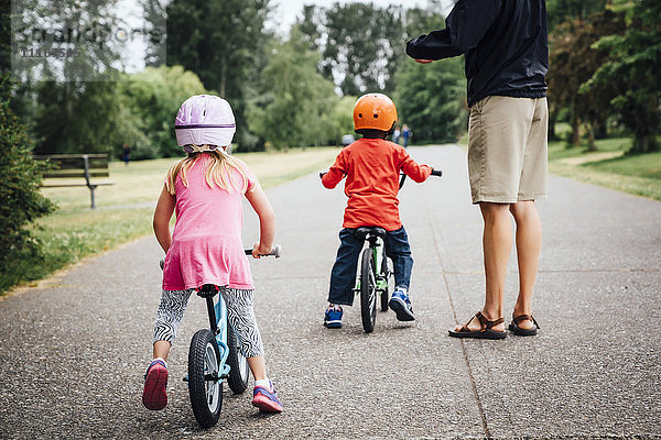 Vater beobachtet Tochter und Sohn beim Fahrradfahren