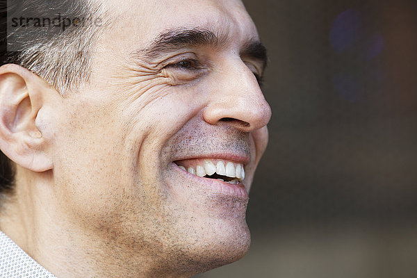 Ein Mann mit grauem Haar in einem Hemd  der zur Seite schaut und lächelt.