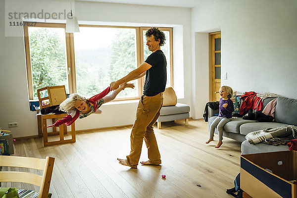 Kaukasischer Vater  der seine Tochter im Wohnzimmer am Arm und am Bein festhält