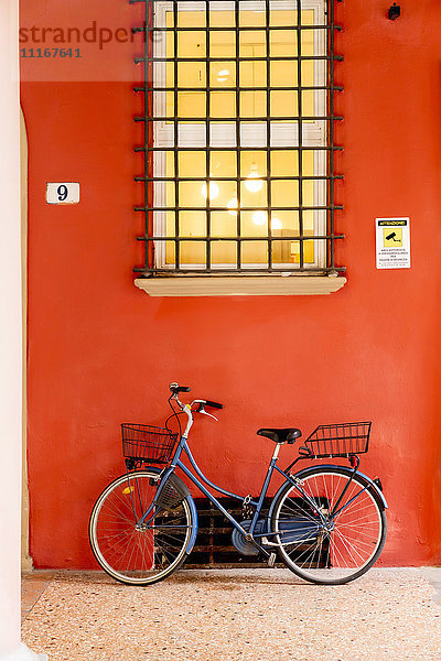 Blaues Fahrrad lehnt an orangefarbener Wand unter Fenster