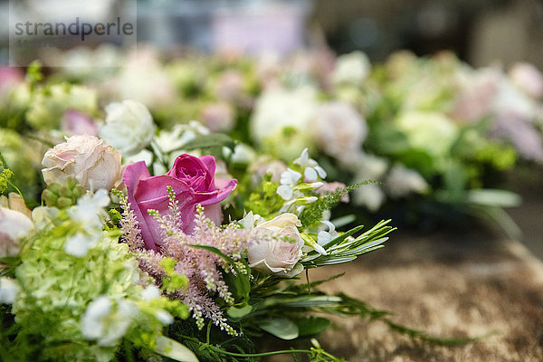 Nahaufnahme von Arrangements auf einer Werkbank. Rosa und weiße Blumen mit grünem Laub.