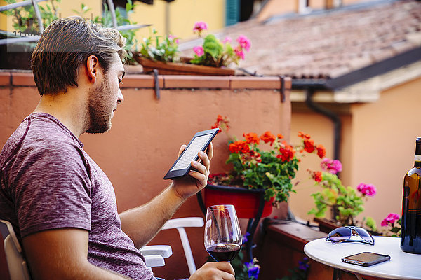 Kaukasischer Mann  der ein digitales Tablet liest und Rotwein trinkt