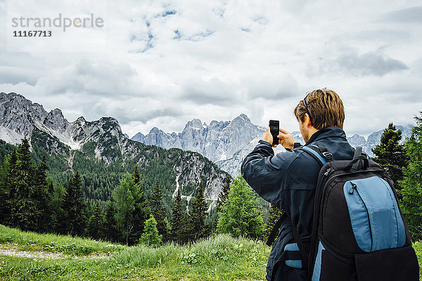 Kaukasischer Mann  der mit seinem Mobiltelefon ein Gebirge fotografiert