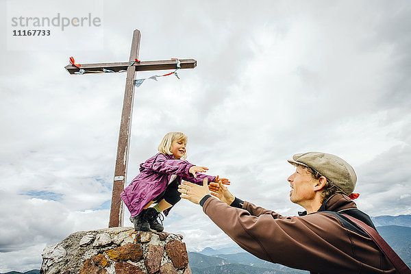 Kaukasischer Vater hilft seiner Tochter auf einem Felsen am Kruzifix