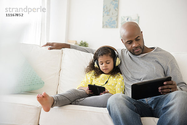 Vater und Tochter benutzen digitale Tablets auf dem Sofa