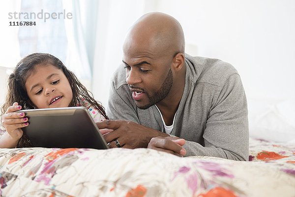 Vater und Tochter benutzen ein digitales Tablet auf dem Bett