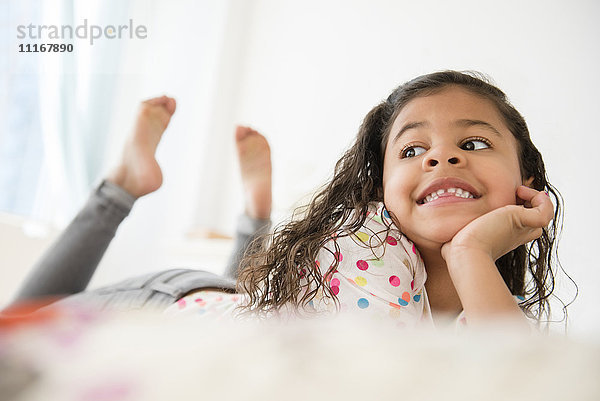 Lächelndes Mixed Race Mädchen auf dem Bett liegend