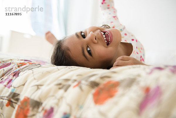 Lächelndes Mixed Race Mädchen rollt auf dem Bett