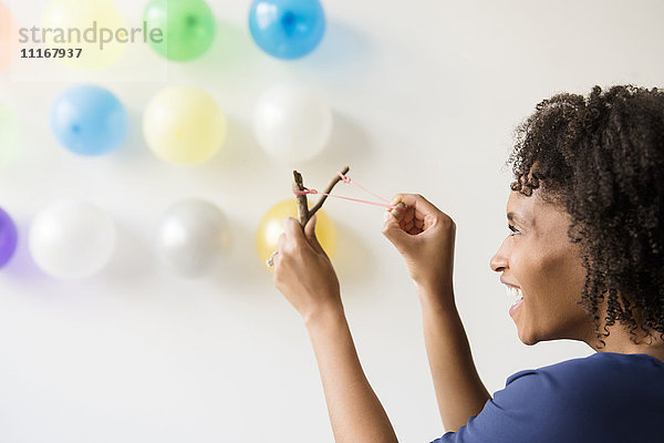 Schwarze Frau zielt mit einer Schleuder auf Luftballons an der Wand