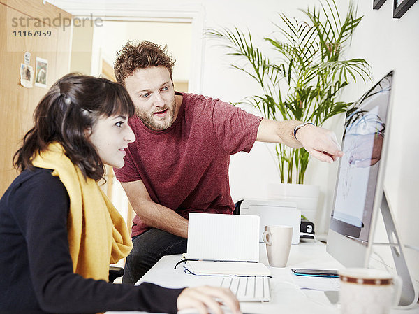 Zwei Menschen arbeiten zusammen in einem Büro und schauen auf einen Computerbildschirm.