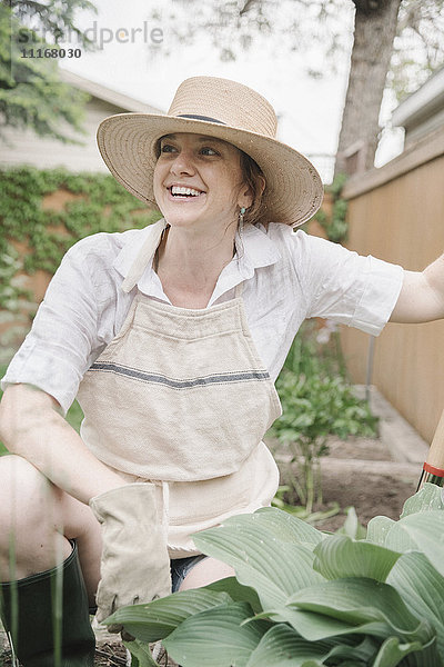 Eine Frau mit einem Strohhut mit breiter Krempe  die in einem Garten arbeitet und gräbt.