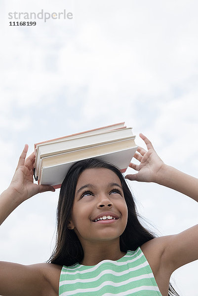 Mixed Race Mädchen balanciert Bücher auf dem Kopf