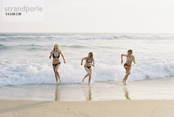 Drei Kinder spielen an einem Sandstrand am Meer.