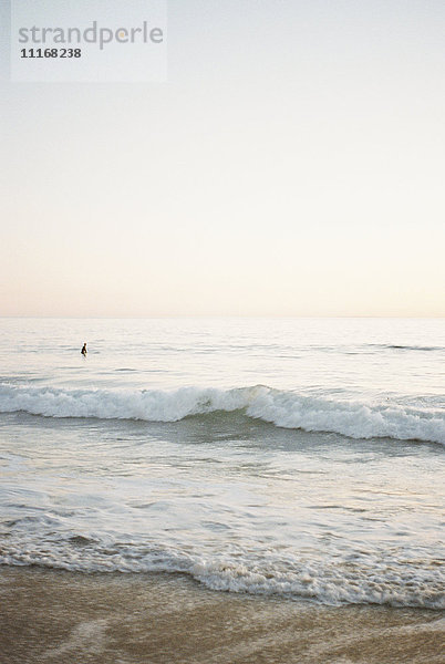 Eine Meereswelle rollt auf einen Sandstrand  im Hintergrund die Person.
