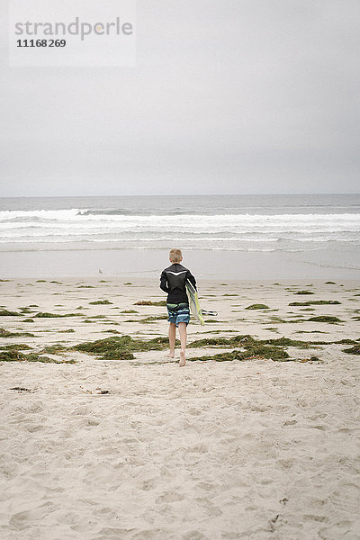 Rückansicht eines Jungen  der ein Bodyboard trägt und in den Ozean geht.