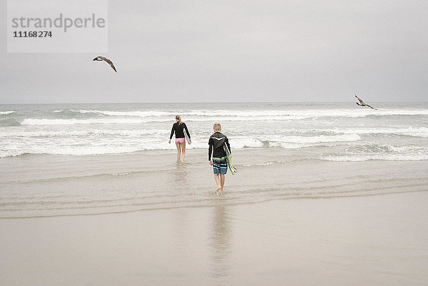 Rückansicht eines Jungen und eines Mädchens  die Bodyboards tragen und in den Ozean gehen.
