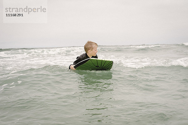 Blonder Junge beim Bodyboarding im Meer.