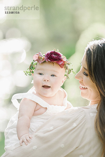 Porträt einer lächelnden Mutter und eines lächelnden Mädchens mit einem Blumenkranz auf dem Kopf.
