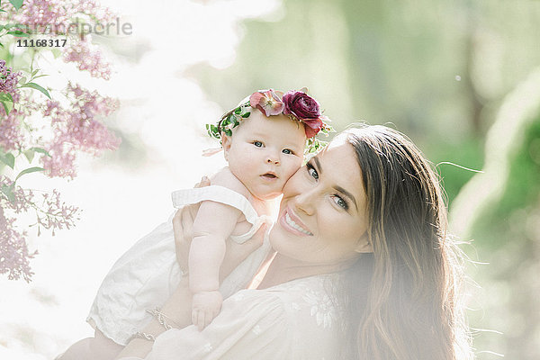 Porträt einer lächelnden Mutter und eines lächelnden Mädchens mit einem Blumenkranz auf dem Kopf.