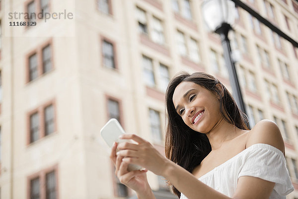 Lächelnde Mixed-Race-Frau  die in der Stadt eine SMS auf ihrem Handy schreibt