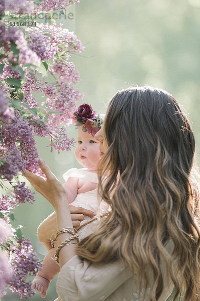 Mutter hält ein kleines Mädchen mit einem Blumenkranz auf dem Kopf.