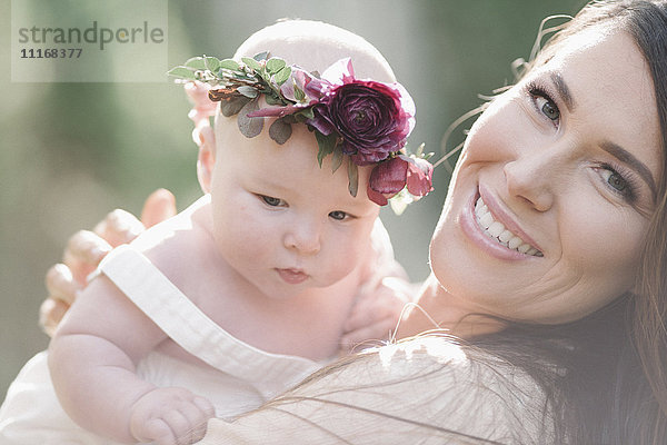Porträt einer lächelnden Mutter und eines lächelnden Mädchens mit einem Blumenkranz auf dem Kopf.