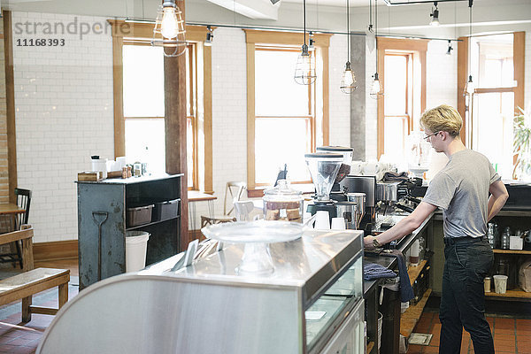 Junger blonder Mann  der an einem Tresen in einem Café steht.