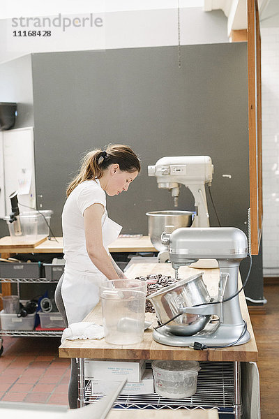 Frau mit weißer Schürze  die an einem Arbeitstresen in einer Bäckerei steht.