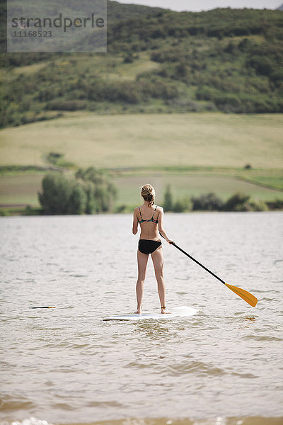 Ein junges Mädchen steht auf und paddelt auf einem See.
