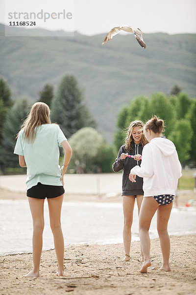 Mädchen im Teenageralter  die an einem Sandstrand an einem See stehen.
