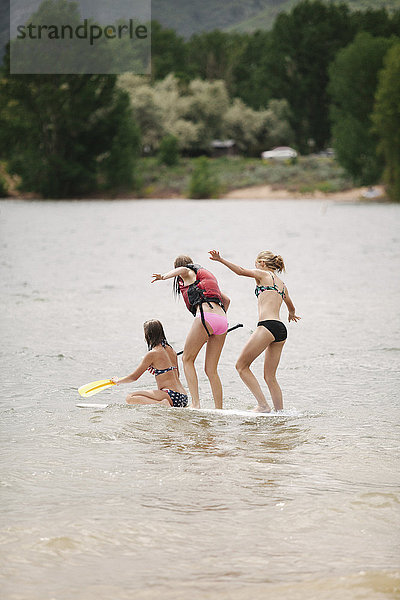 Drei Mädchen im Teenageralter auf einem Paddelbrett auf einem See.