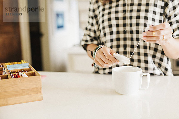 Frau trägt ein kariertes Hemd und macht eine Tasse Tee.