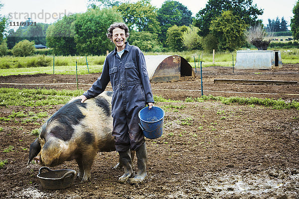 Eine Frau stand neben einem großen Schwein  das einen Eimer hielt.