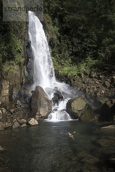 Gemischtrassige Frau schwimmt im Wasserfall-Pool