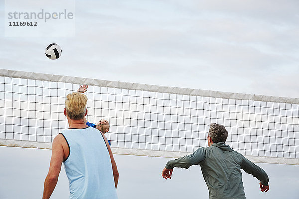 Ältere Männer stehen am Strand und spielen Beach-Volleyball.