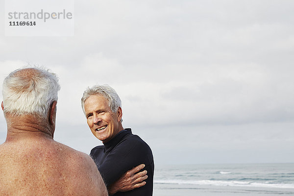 Zwei ältere Männer stehen am Strand und unterhalten sich  einer trägt einen Neoprenanzug.