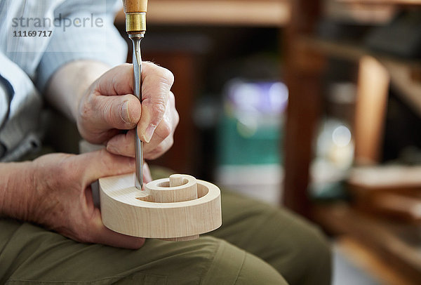 Ein Geigenbauer  der mit Handwerkzeugen eine neue hölzerne Geigenkopfplatte glättet und fertigstellt  gewellte Schnecke aus Holz.
