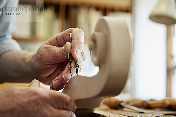 Ein Geigenbauer  der in seiner Werkstatt arbeitet und mit Handwerkzeugen die gewellte Schnecke des Geigenschaftes formt und ziseliert.