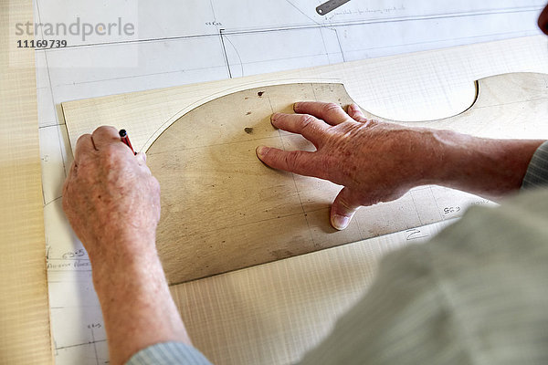 Die Werkstatt eines Geigenbauers. Geschickter Handwerker  der um den Umriss eines Holzbodens für eine Geige zeichnet.