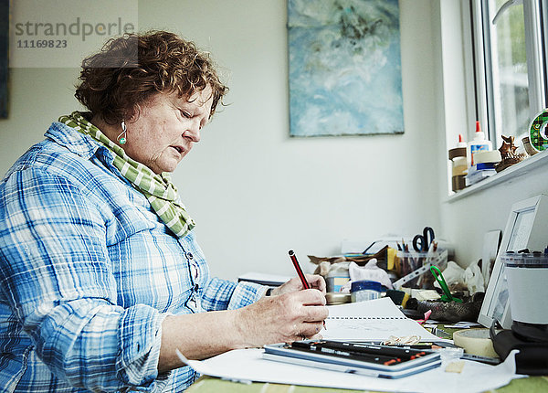 Eine Künstlerin  die an einem Tisch arbeitet und eine Bleistiftzeichnung auf Papier hält.