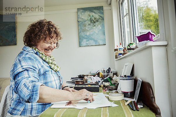 Eine Künstlerin  die an einem Tisch arbeitet  einen großen blauen Pastellstift benutzt und auf Papier zeichnet.