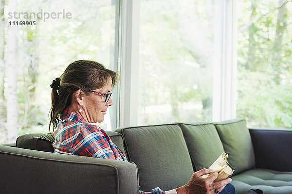 Eine Frau im Karohemd  die auf einem Sofa sitzt und ein Buch liest.