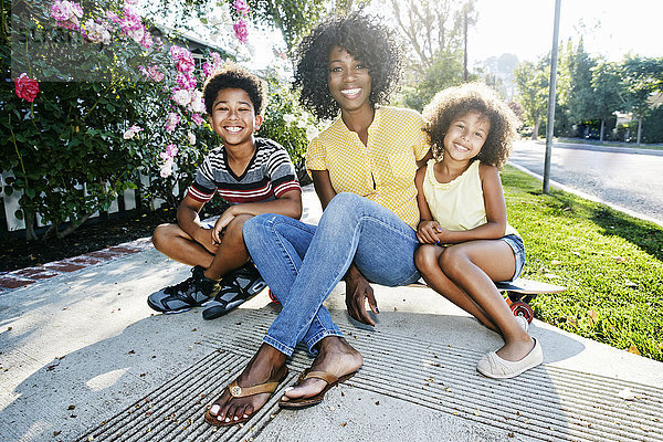 Lächelnde Mutter und Kinder sitzen auf dem Skateboard auf dem Bürgersteig