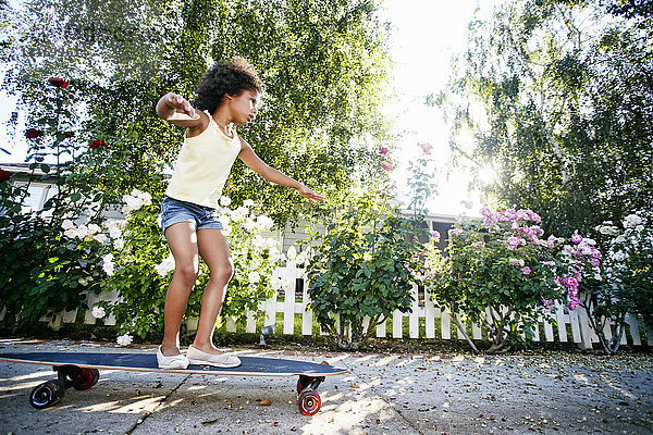 Mixed Race Mädchen skateboarding auf dem Bürgersteig