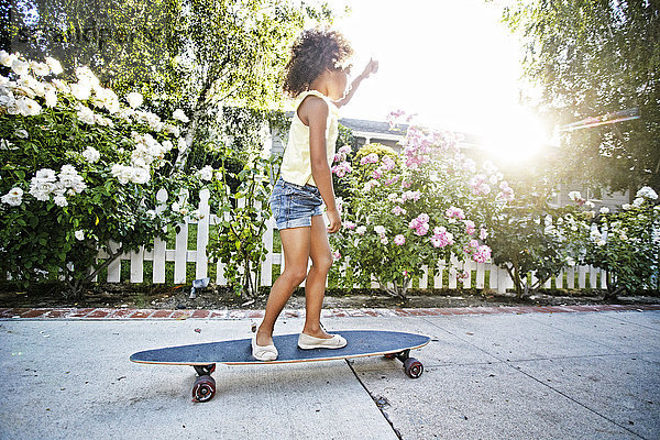 Mixed Race Mädchen skateboarding auf dem Bürgersteig