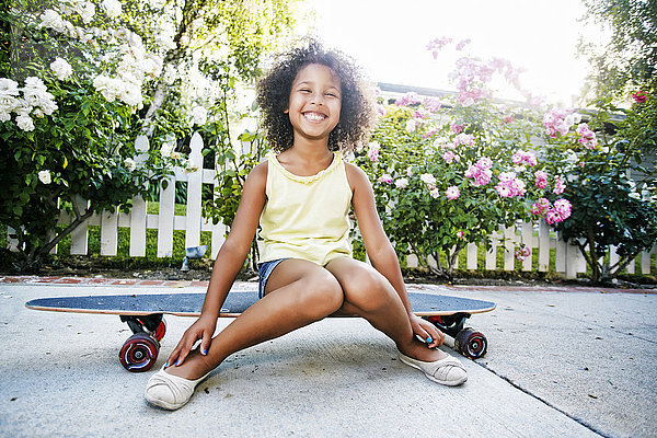 Lächelndes Mixed Race Mädchen auf Skateboard sitzend