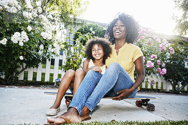 Lächelnde Mutter und Tochter sitzen auf einem Skateboard