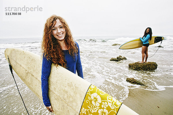 Lächelnde Frauen mit Surfbrettern am Strand