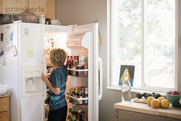 Familie bereitet das Frühstück in einer Küche vor  Junge steht an einem offenen Kühlschrank.