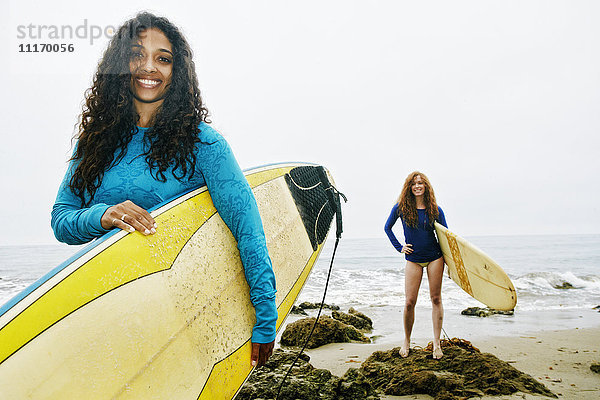 Lächelnde Frauen mit Surfbrettern am Strand